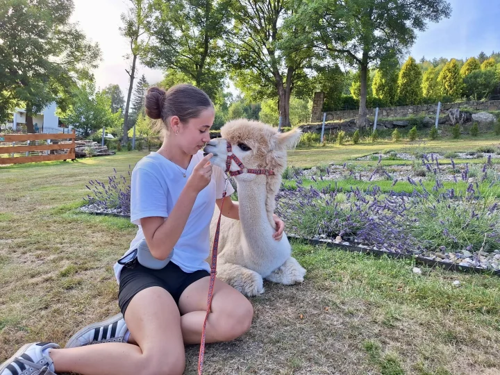 A woman is sitting on the grass next to an alpaca during a photo shoot